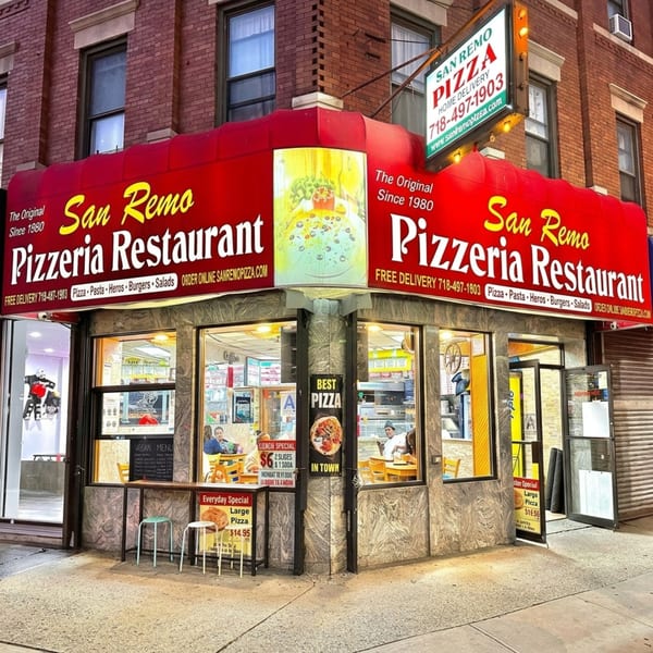San Remo Pizzeria Restaurant, a corner building with red awnings and illuminated signs, at dusk.