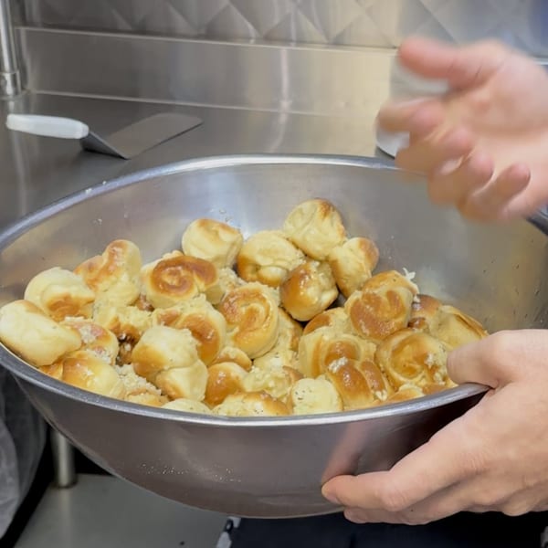 Hands holding a large metal bowl filled with golden-brown garlic knots at San Remo Pizzeria.