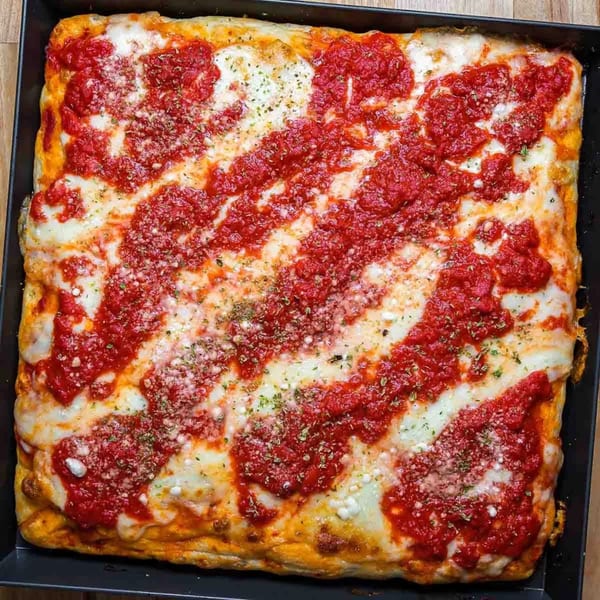 A rectangular San Remo Pizzeria pizza with melted cheese, red sauce stripes, and herbs in a pan.
