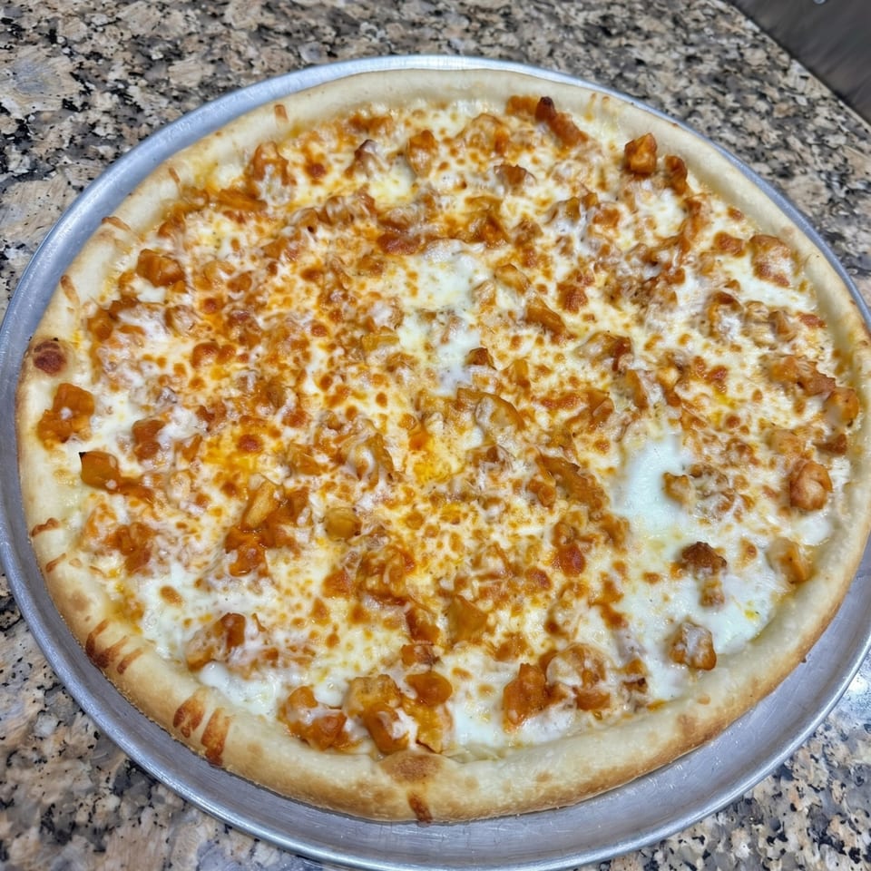 A freshly baked buffalo chicken pizza with white sauce and melted cheese on a metal pan.